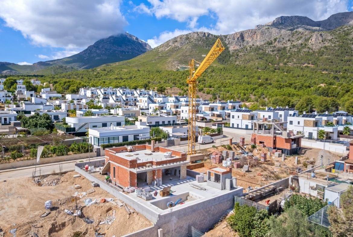 Expansive luxury 5-bedroom villa under construction in Polop de la Marina, set against dramatic mountain backdrop and lush greenery.