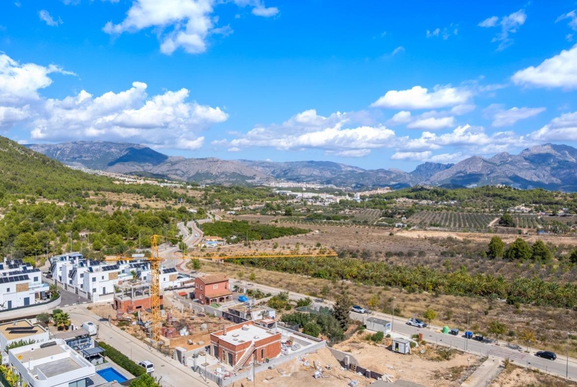 Expansive aerial view of a luxury villa construction site in Polop de la Marina, surrounded by lush mountains and open landscapes.