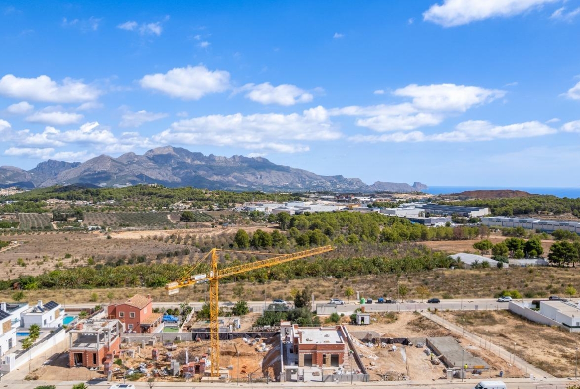Expansive construction site of a spacious luxury 5-bedroom villa in Polop de la Marina with panoramic sea and mountain views under a clear sky.
