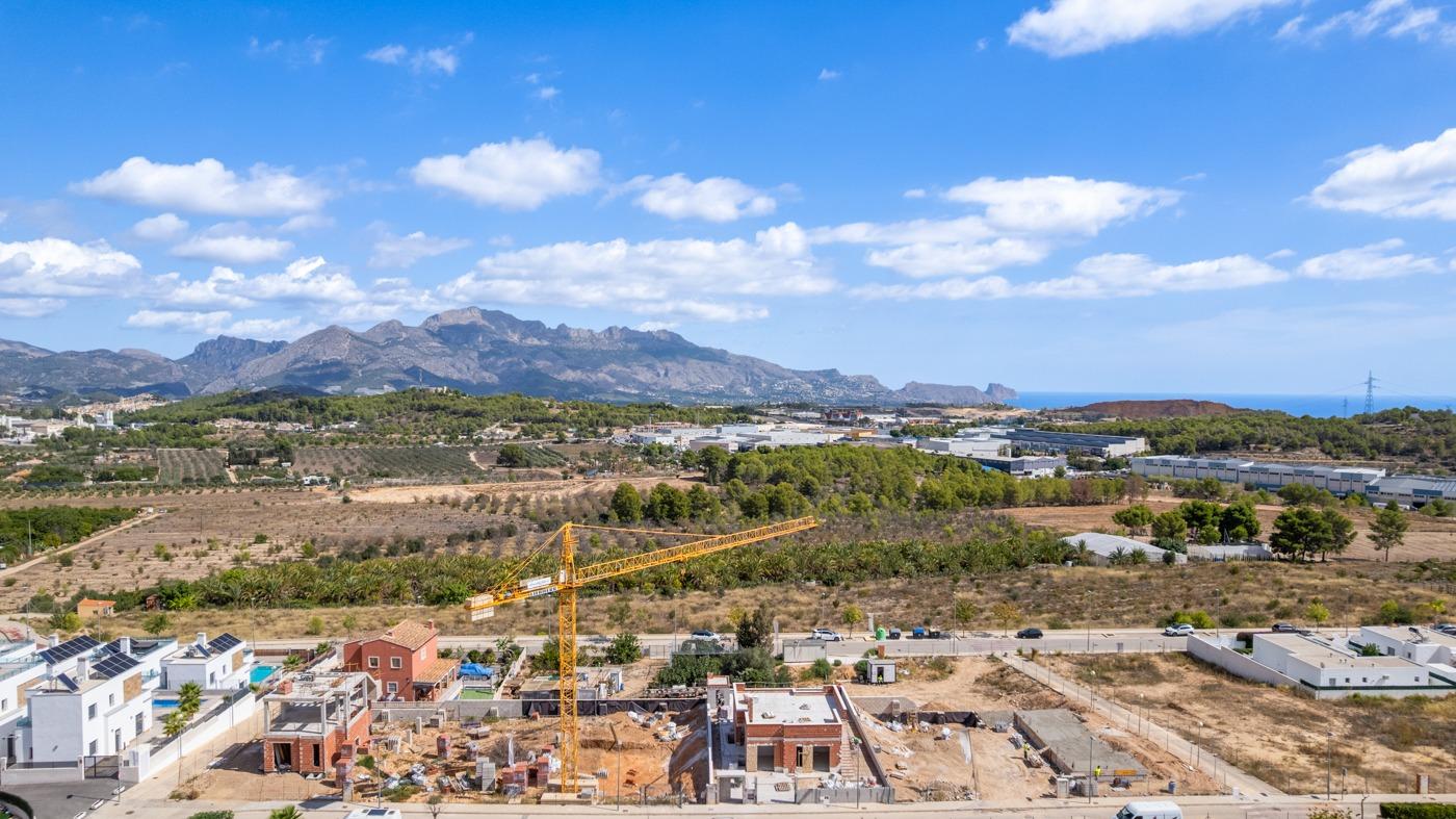 Expansive construction site of a spacious luxury 5-bedroom villa in Polop de la Marina with panoramic sea and mountain views under a clear sky.