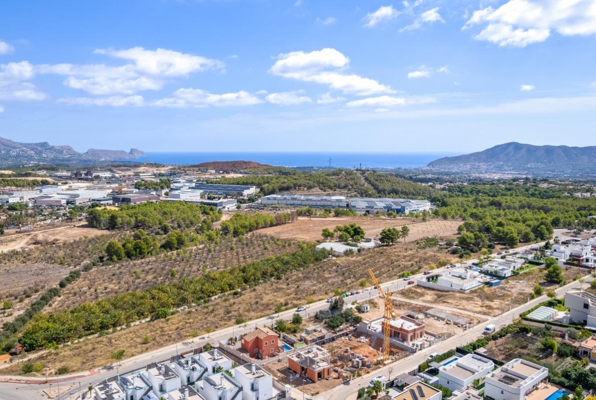 Aerial view of spacious luxury villa under construction in Polop de la Marina, surrounded by greenery with sea and mountain vistas.