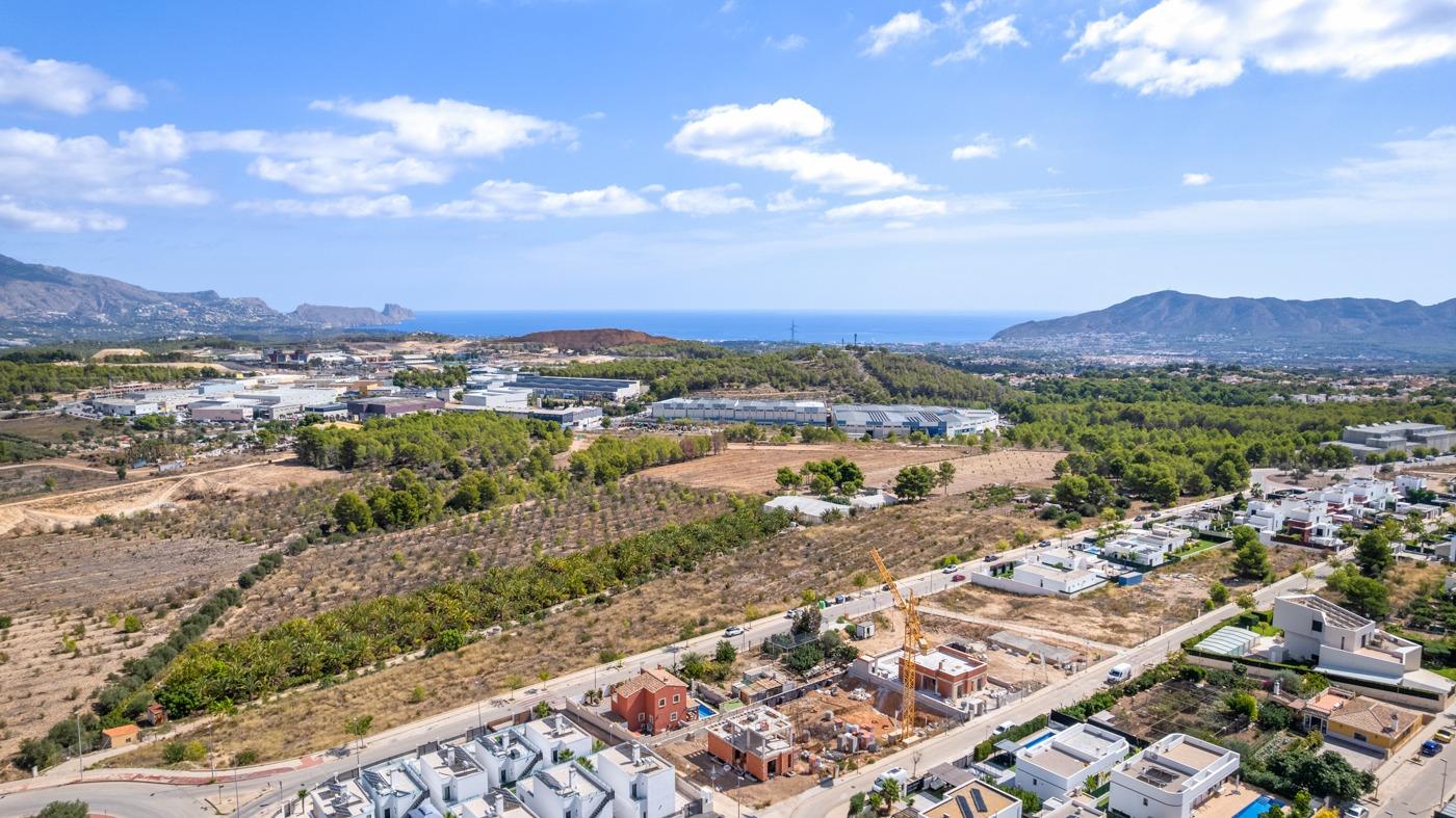 Aerial view of spacious luxury villa under construction in Polop de la Marina, surrounded by greenery with sea and mountain vistas.