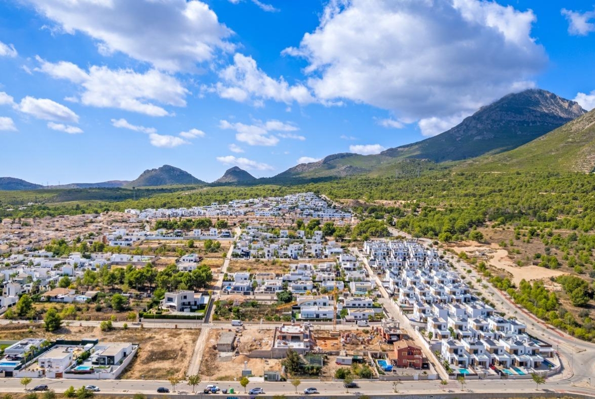 Panoramic aerial view of a luxury villa development with modern white homes in Polop de la Marina, surrounded by mountains.