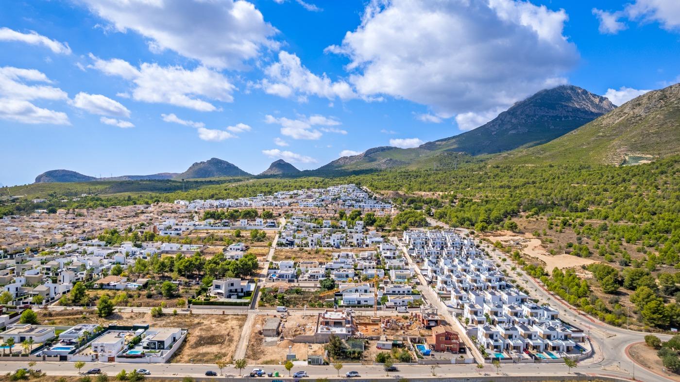 Panoramic aerial view of a luxury villa development with modern white homes in Polop de la Marina, surrounded by mountains.