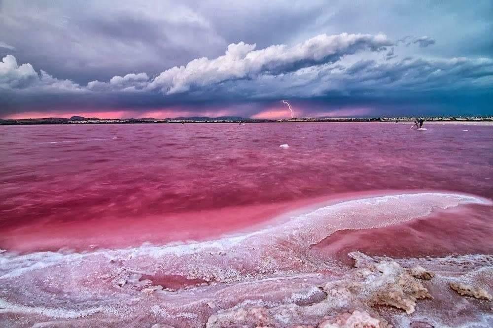 Vibrant pink salt lake with dramatic storm clouds and lightning near spacious new build 2-bedroom apartment in central Torrevieja.
