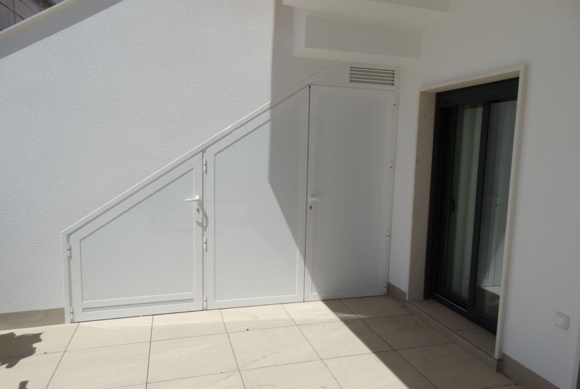 Bright, modern exterior corner with sleek white storage doors and tiled terrace in new build bungalows, Pilar de la Horadada.
