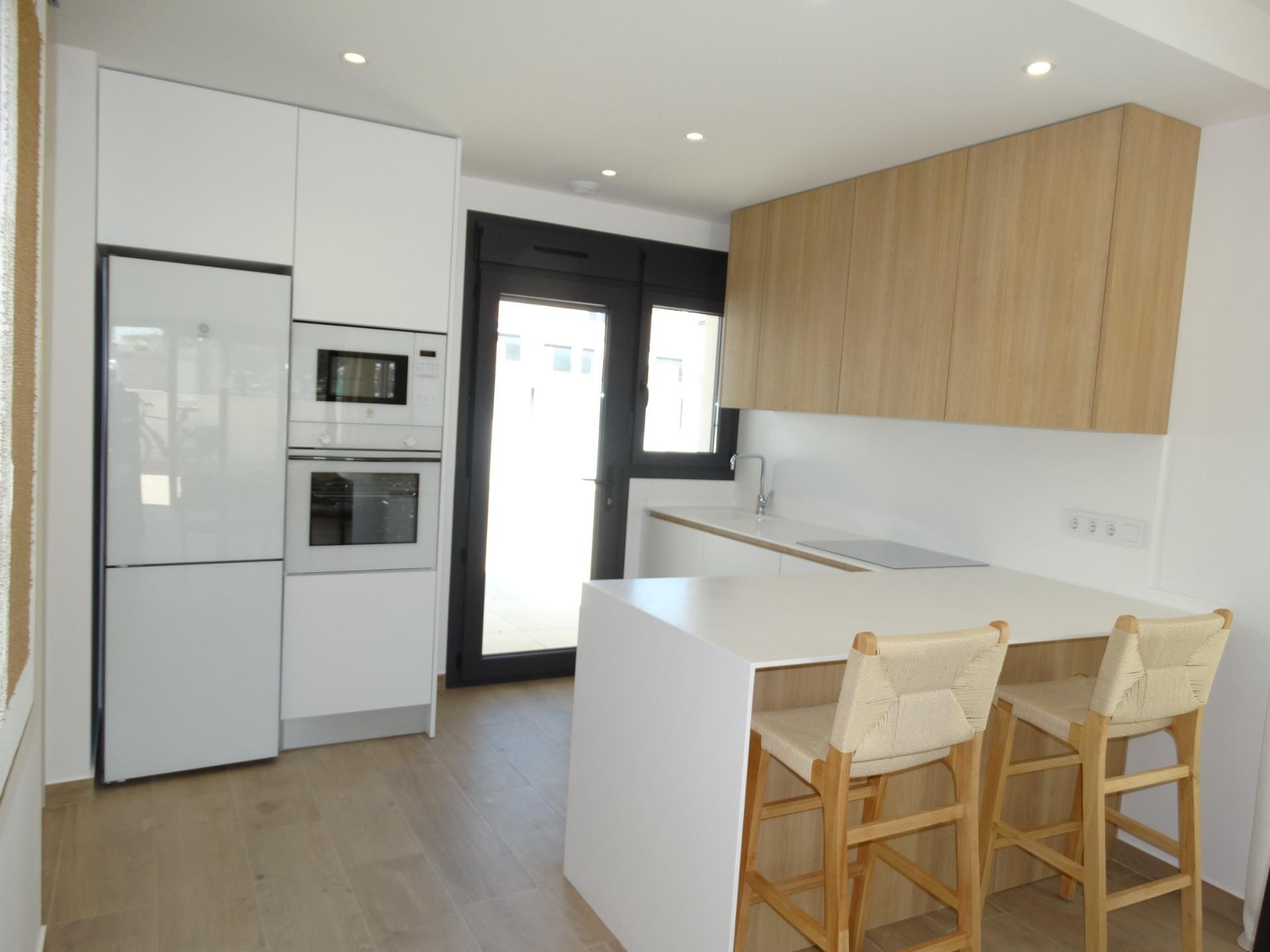 Bright modern kitchen with sleek cabinetry and breakfast bar in new build bungalows, Pilar de la Horadada.