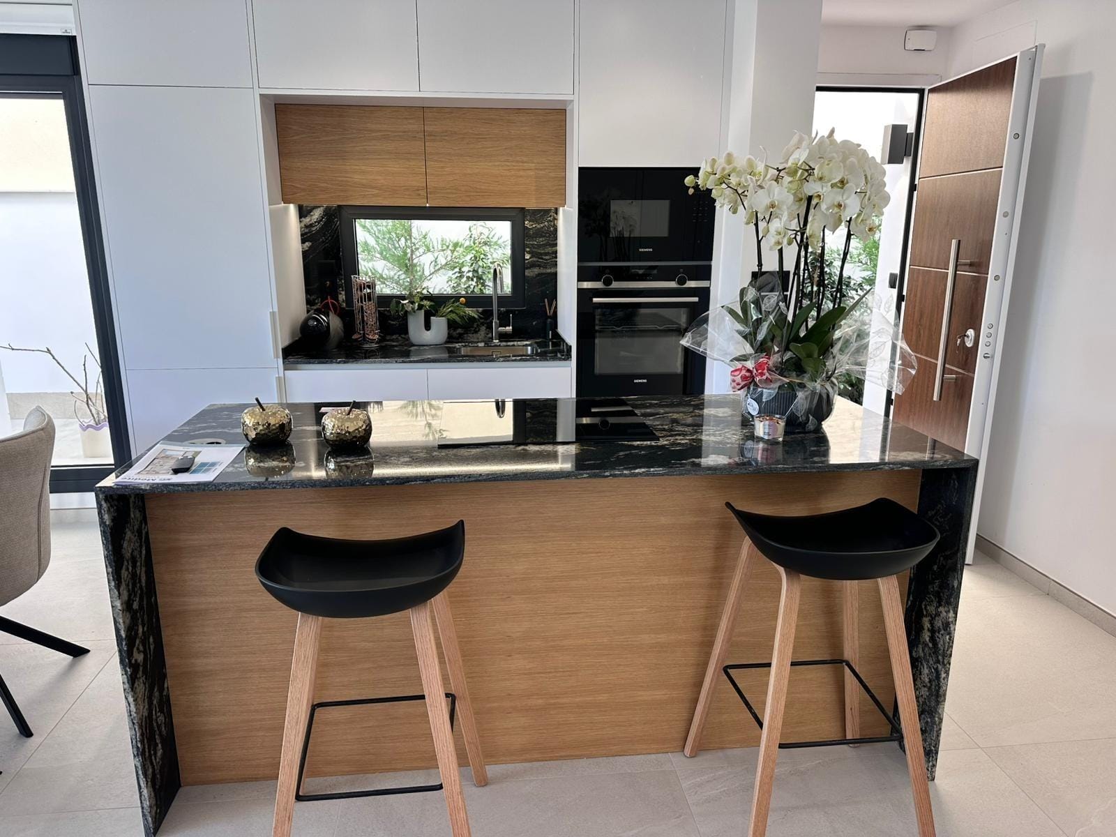 Modern-New-Build-Villas-for-Sale-in-San-Pedro-del-Pinatar-–-Close-to-Beach-and-Town-Centre-10 Modern sunlit kitchen with sleek black granite island and wooden accents in key-ready villa, San Pedro del Pinatar, Costa Cálida
