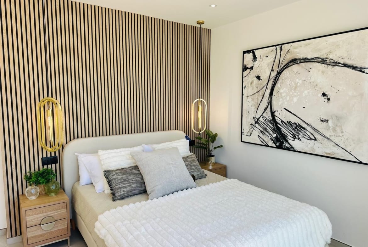 Bright modern bedroom with elegant wood paneling, gold pendant lights, and abstract art in a luxury villa in San Pedro del Pinatar.