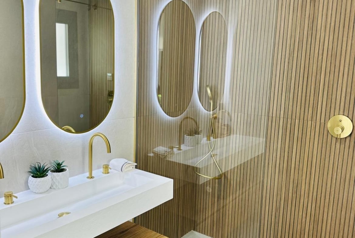 Modern luxury bathroom with illuminated oval mirrors, gold fixtures, and sleek wooden accents in San Pedro del Pinatar villa.
