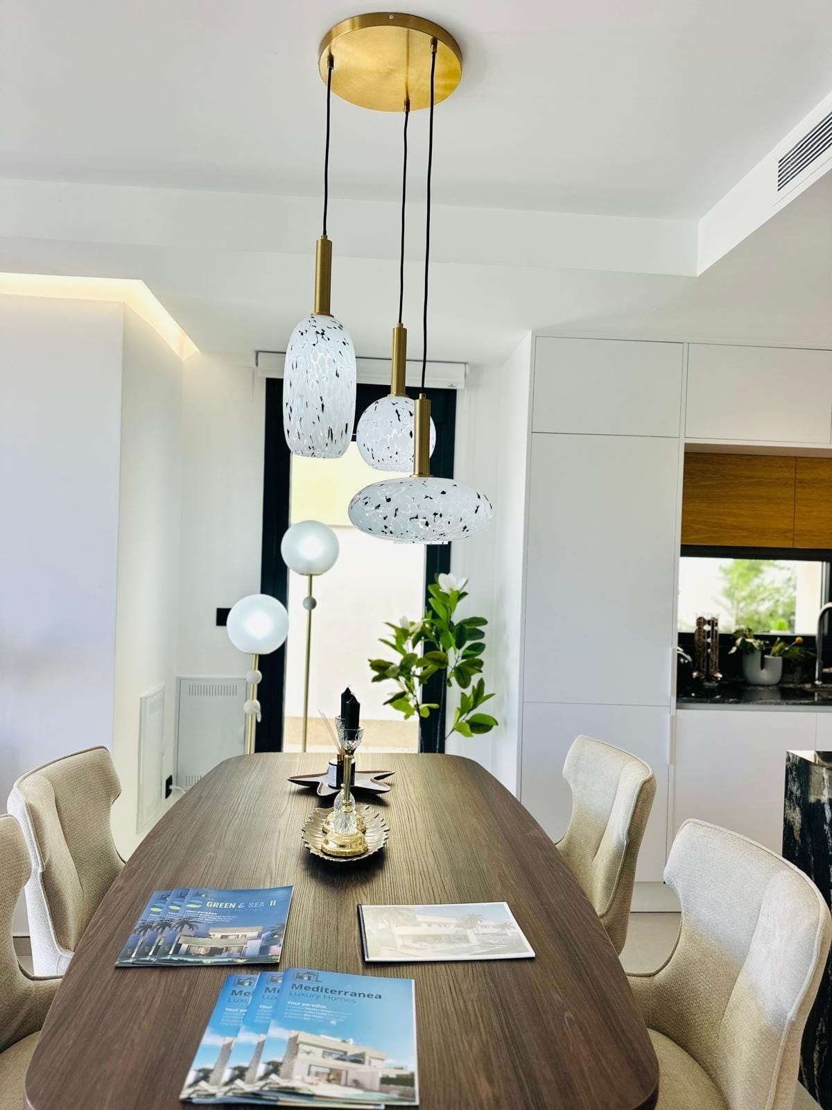 Modern-New-Build-Villas-for-Sale-in-San-Pedro-del-Pinatar-–-Close-to-Beach-and-Town-Centre-7 Elegant dining area with modern pendant lights, plush chairs, and sleek kitchen in new build villa in San Pedro del Pinatar, Costa Cálida