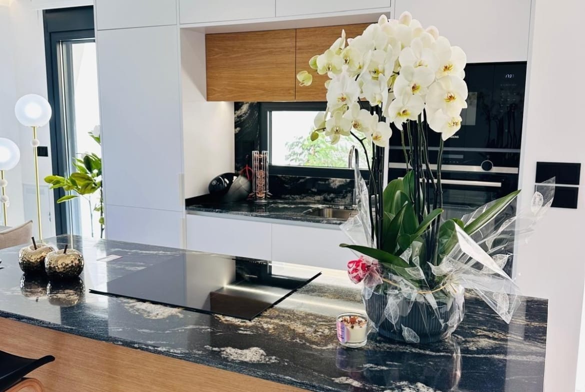 Modern kitchen with sleek granite island, elegant white cabinetry, and vibrant orchid centerpiece in San Pedro del Pinatar villa.