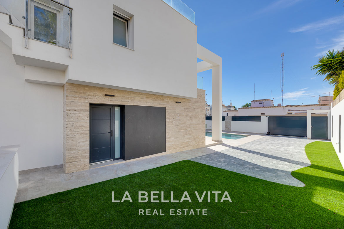 Modern villa with private pool, solarium and basement near La Mata beach, Torrevieja-03 Modern four-bedroom villa exterior in Torreblanca, Torrevieja featuring a sleek facade, private pool, and landscaped sunlit courtyard.