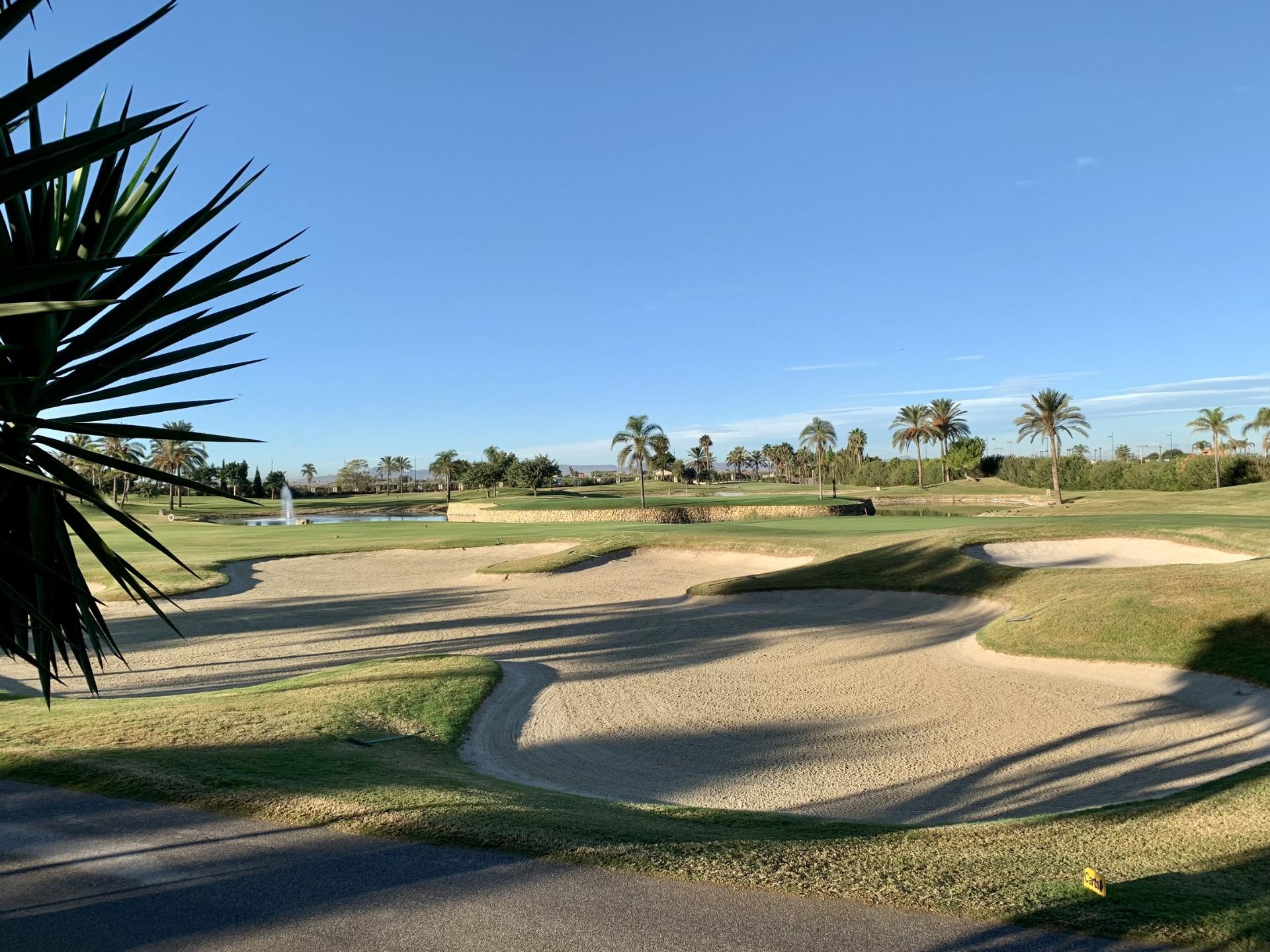 Expansive sun-drenched golf course with manicured greens and palm trees at luxury modern penthouse in Roda Golf, San Javier.