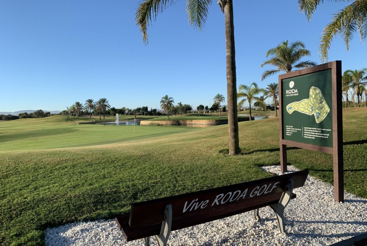 Sunlit golf course overview with lush greens and palm trees near a bench, highlighting the serene setting of Roda Golf, San Javier bungalow.