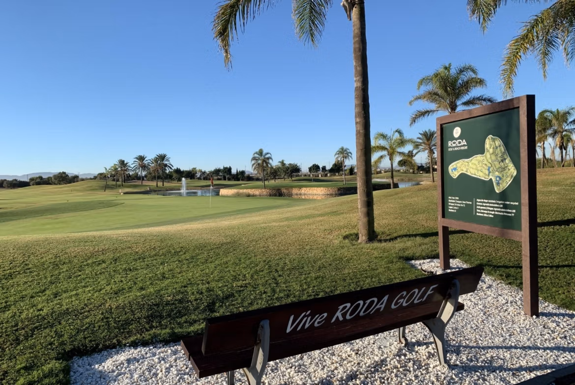 Sunlit golf course overview with lush greens and palm trees near a bench, highlighting the serene setting of Roda Golf, San Javier bungalow.