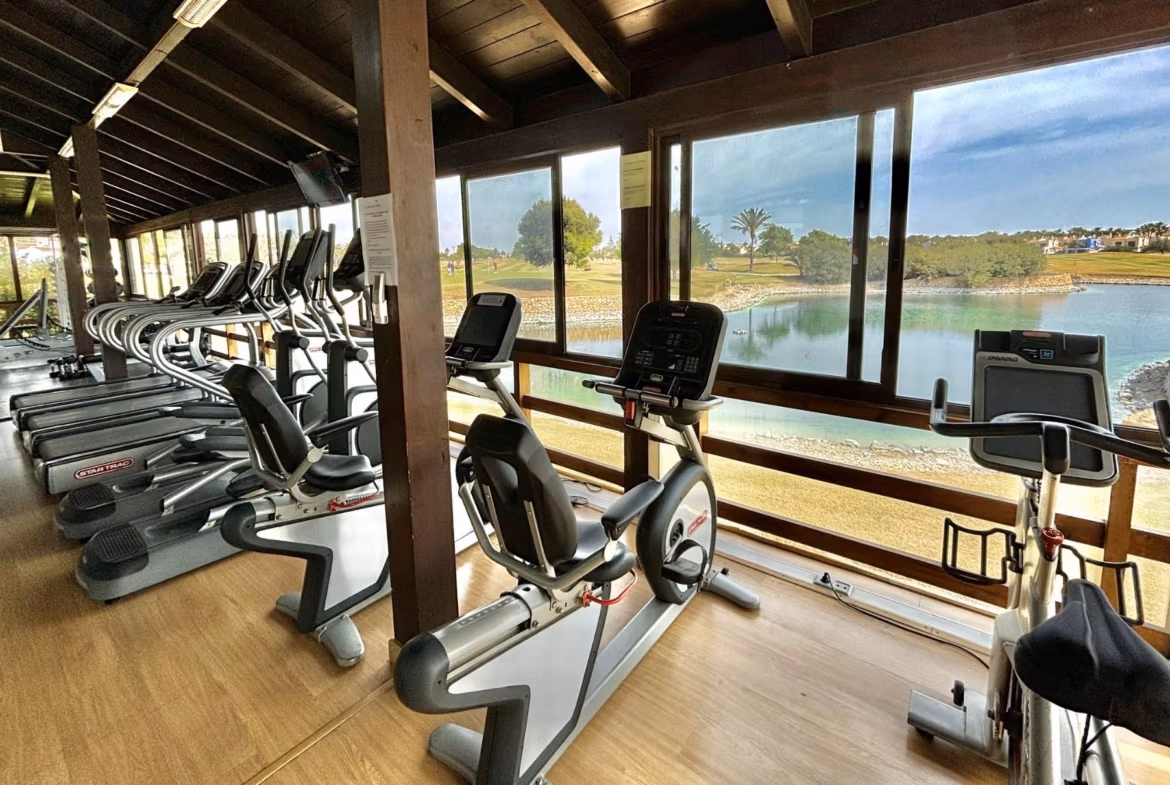 Bright, spacious gym with modern cardio equipment overlooking a serene lake at Roda Golf, San Javier near the new 3-bedroom bungalow.