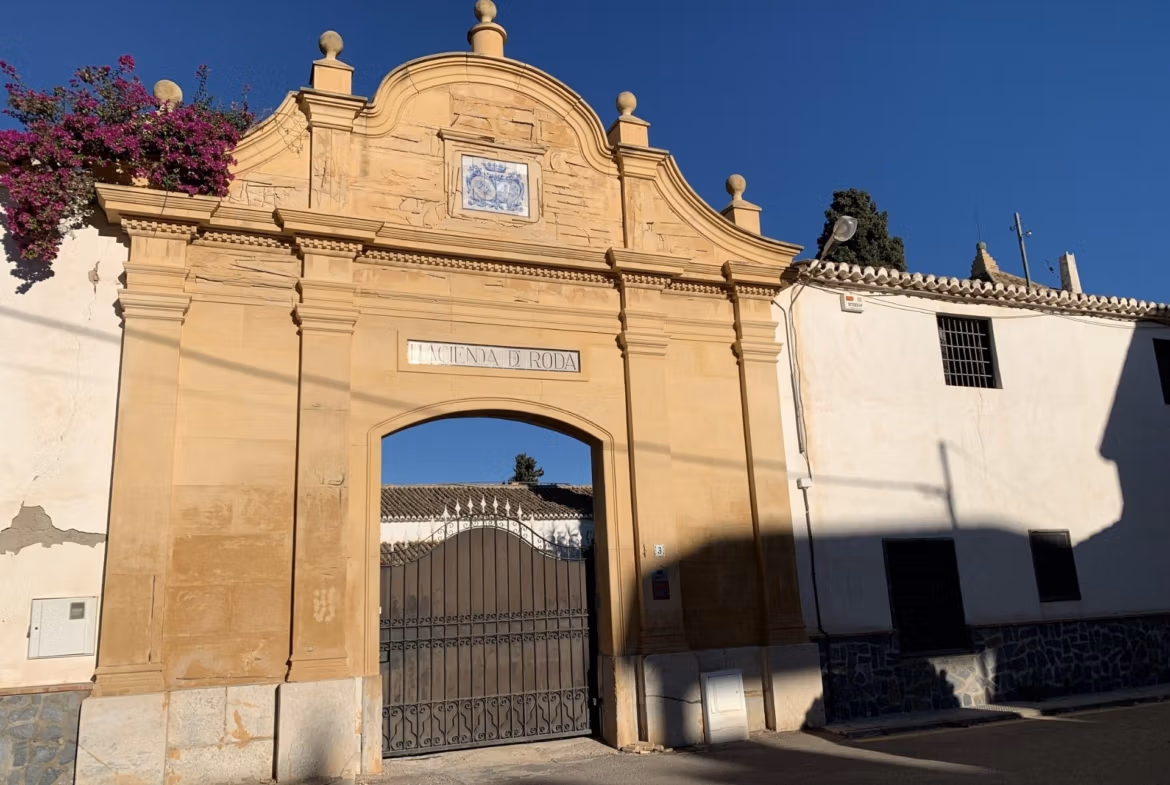 Elegant historic stone archway entrance framed by vibrant pink bougainvillea under a clear blue sky at Roda Golf, San Javier.