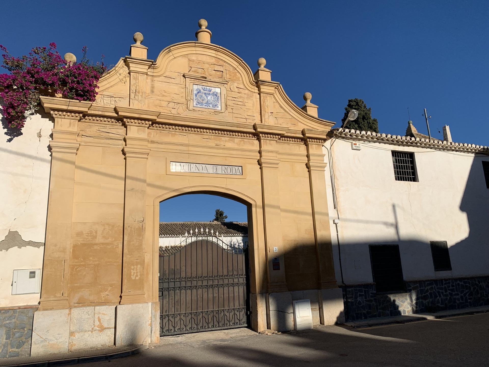 Elegant historic stone archway entrance framed by vibrant pink bougainvillea under a clear blue sky at Roda Golf, San Javier.