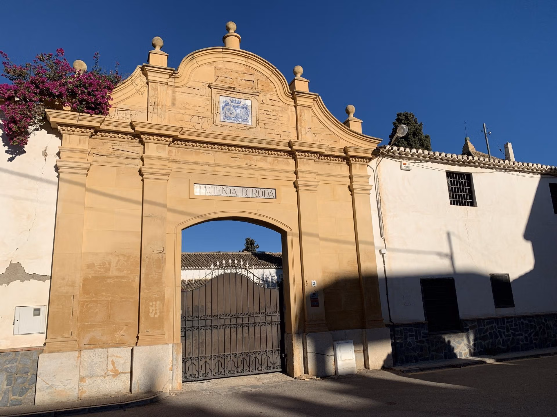 Elegant historic stone archway entrance framed by vibrant pink bougainvillea under a clear blue sky at Roda Golf, San Javier.