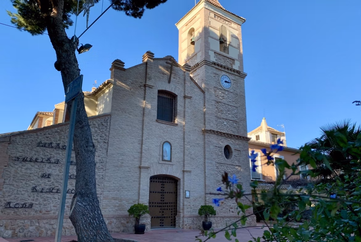 Historic rustic church with bright stone façade and clock tower near Roda Golf, San Javier, surrounded by greenery.