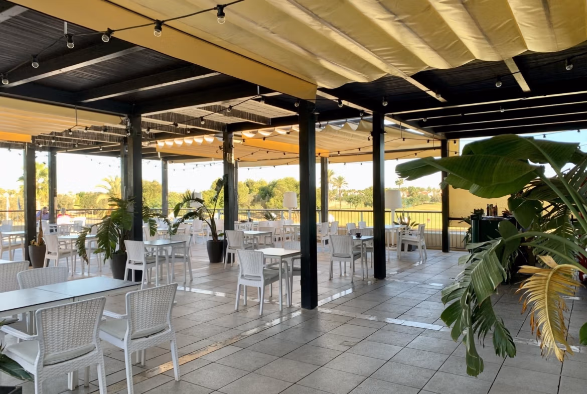 Spacious covered terrace with modern white dining set and views over lush golf course at bungalow in Roda Golf, San Javier