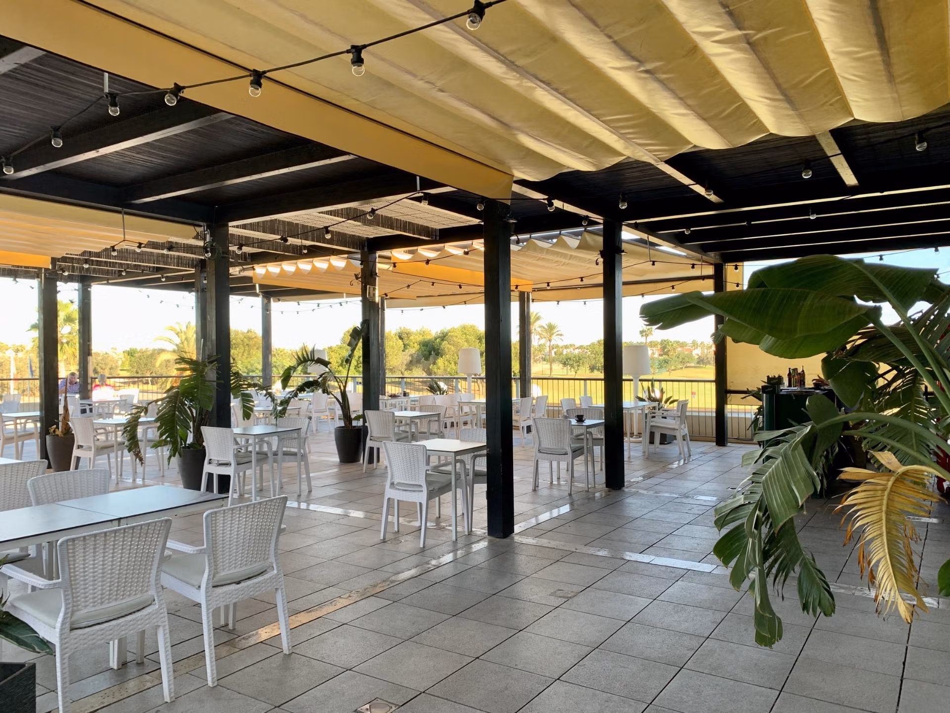 Spacious covered terrace with modern white dining set and views over lush golf course at bungalow in Roda Golf, San Javier