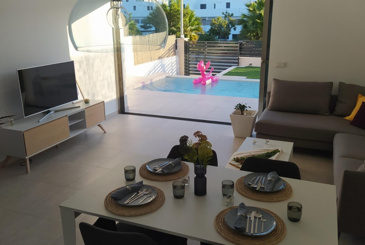Bright modern open-plan living and dining area with sleek furnishings overlooking a private pool in a 3-bedroom villa in Villamartin.