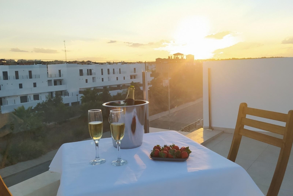 Sunlit terrace of a modern 3 bedroom villa in Villamartin, Orihuela Costa, featuring a cozy dining setup with champagne and strawberries.