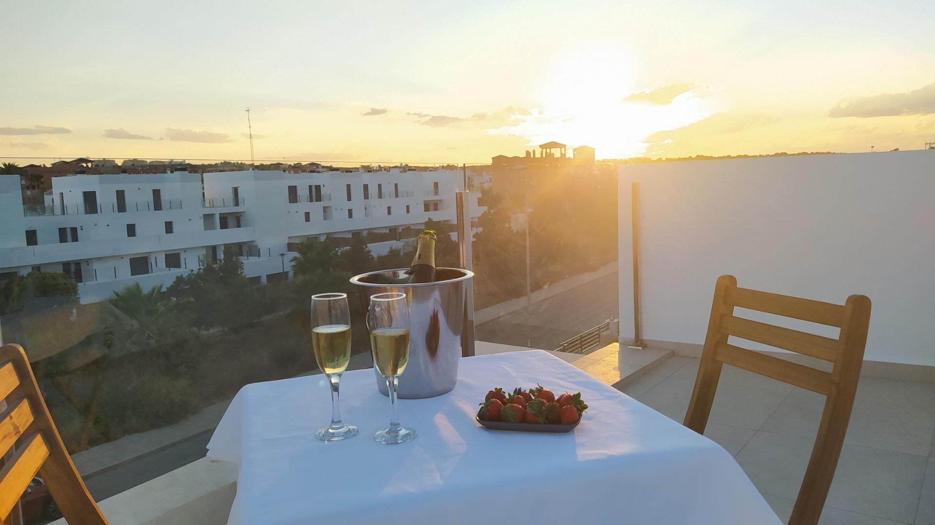 Sunlit terrace of a modern 3 bedroom villa in Villamartin, Orihuela Costa, featuring a cozy dining setup with champagne and strawberries.