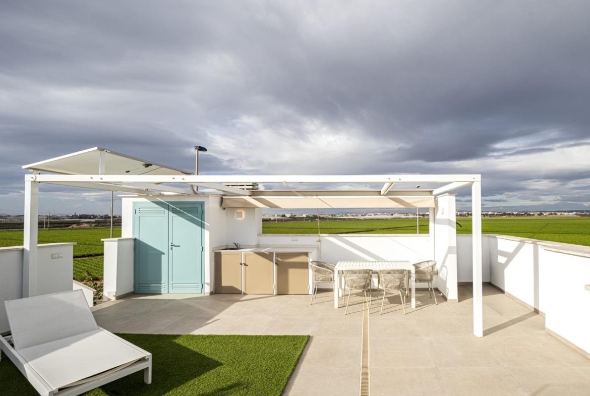 NEW-BUILD-RESIDENTIAL-COMPLEX-IN-TORRE-DE-LA-HORADADA-31 Bright top floor solarium with modern pergola, dining area, sun loungers, and scenic green views in Torre de la Horadada luxury apartment.