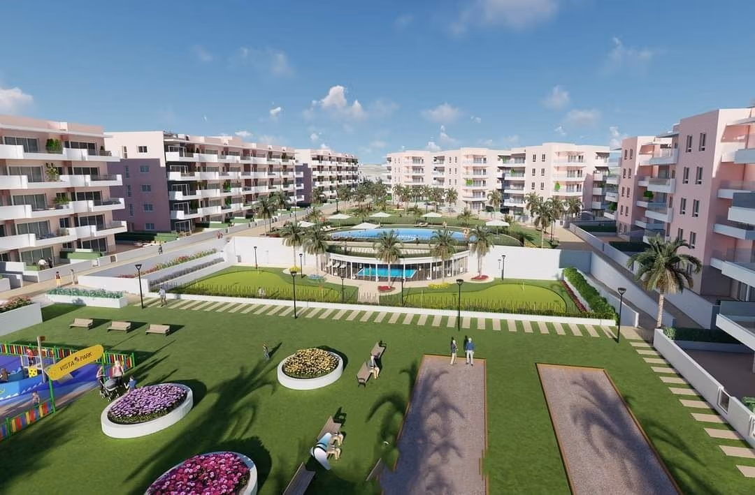 Modern communal garden with landscaped lawns, children's play area, and pool in luxury ground floor apartment complex in El Raso, Guardamar del Segura.