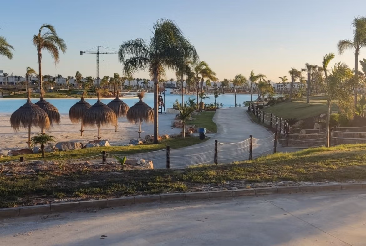Sun-drenched landscaped lakeside view with palm trees and palapas near the luxury 3-bedroom penthouse at Santa Rosalía Lake and Life Resort