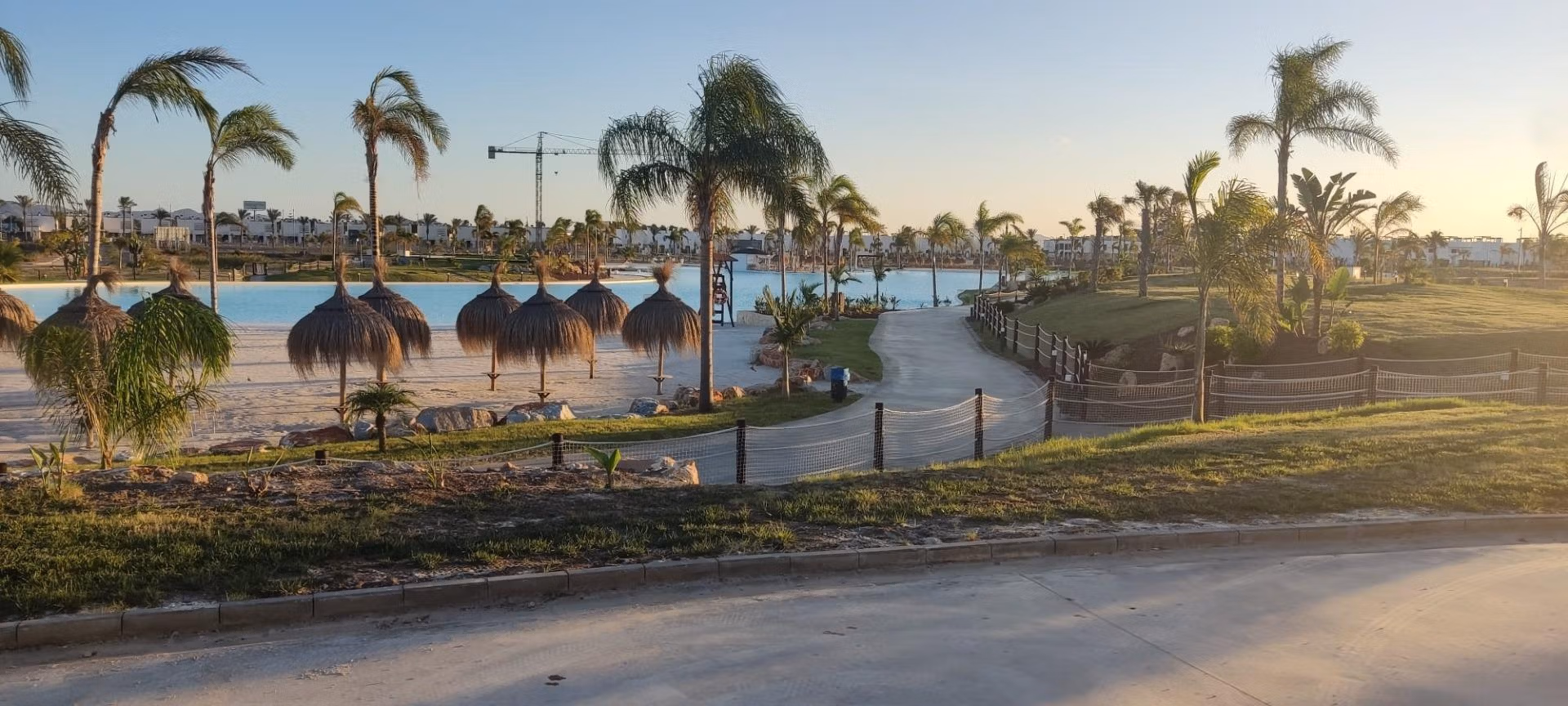 NEW-BUILD-RESIDENTIAL-IN-PRIVATE-GATED-RESORT-IN-PROVINCE-OF-MURCIA-15 Sun-drenched landscaped lakeside view with palm trees and palapas near the luxury 3-bedroom penthouse at Santa Rosalía Lake and Life Resort