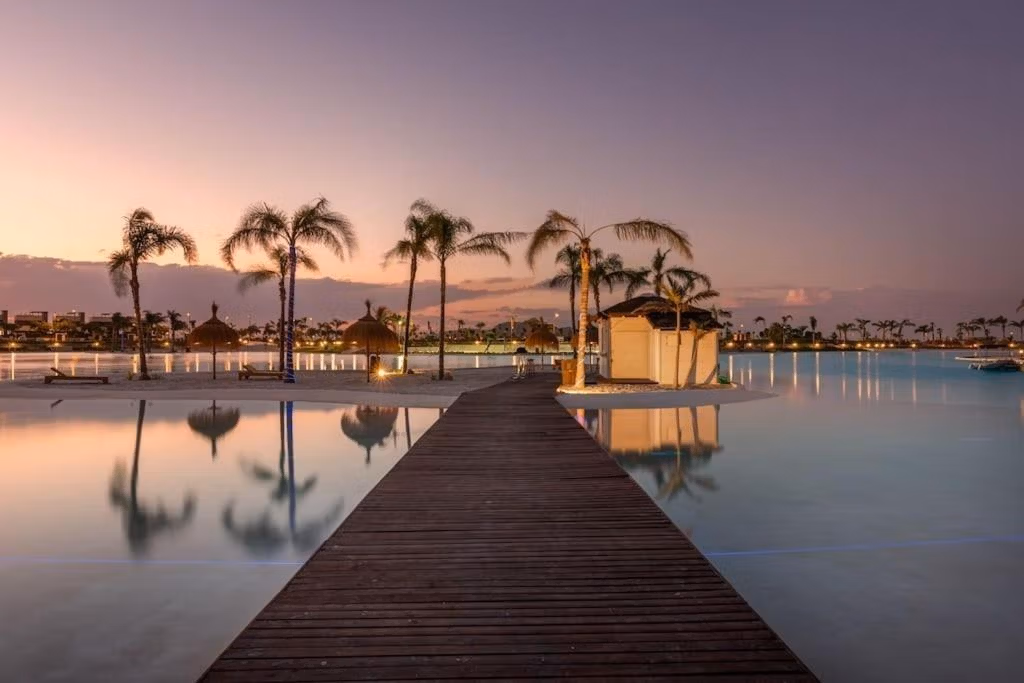 Tranquil sunset view of the expansive infinity pool and palm-fringed walkway at Santa Rosalía Lake and Life Resort penthouse.