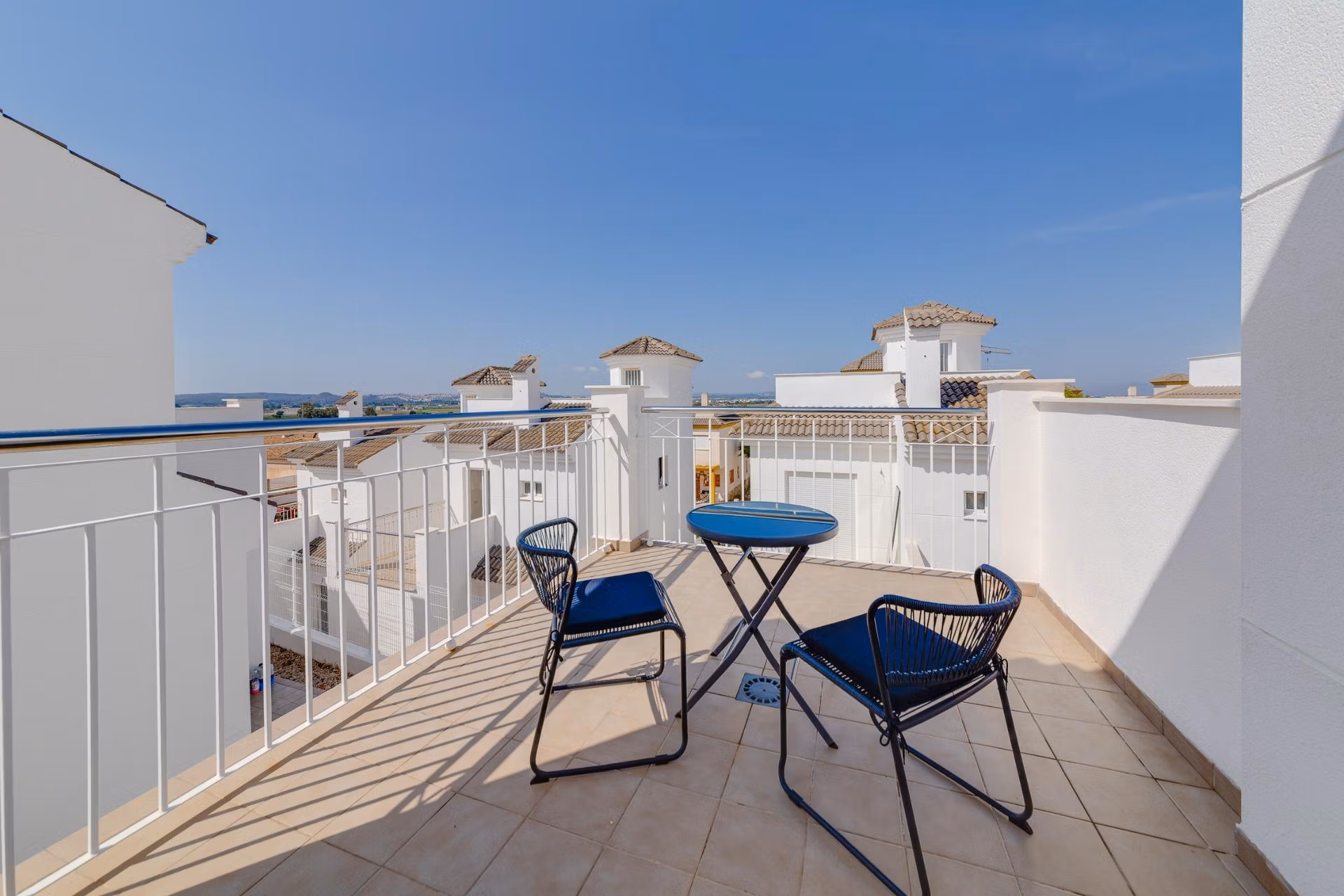 NEW-BUILD-RESIDENTIAL-IN-SAN-FULGENCIO-24 Sunlit solarium terrace with sleek black chairs and table, overlooking whitewashed rooftops of a 3-bedroom villa in El Oasis, San Fulgencio.