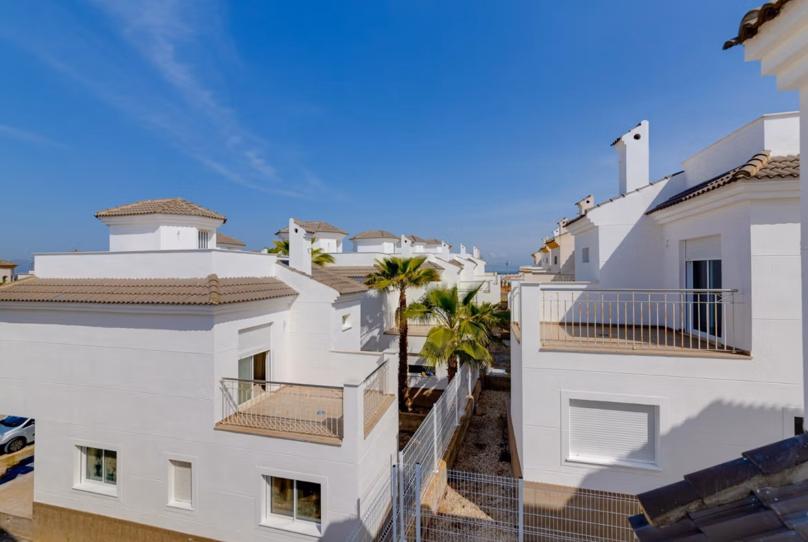 NEW-BUILD-RESIDENTIAL-IN-SAN-FULGENCIO-36 Bright, modern 2 bedroom semi-detached villa exterior in El Oasis La Marina with sunlit terraces and pristine white facades under clear blue skies.