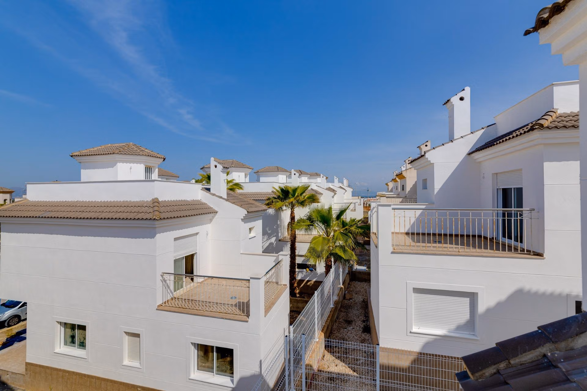 NEW-BUILD-RESIDENTIAL-IN-SAN-FULGENCIO-36 Bright, modern 2 bedroom semi-detached villa exterior in El Oasis La Marina with sunlit terraces and pristine white facades under clear blue skies.