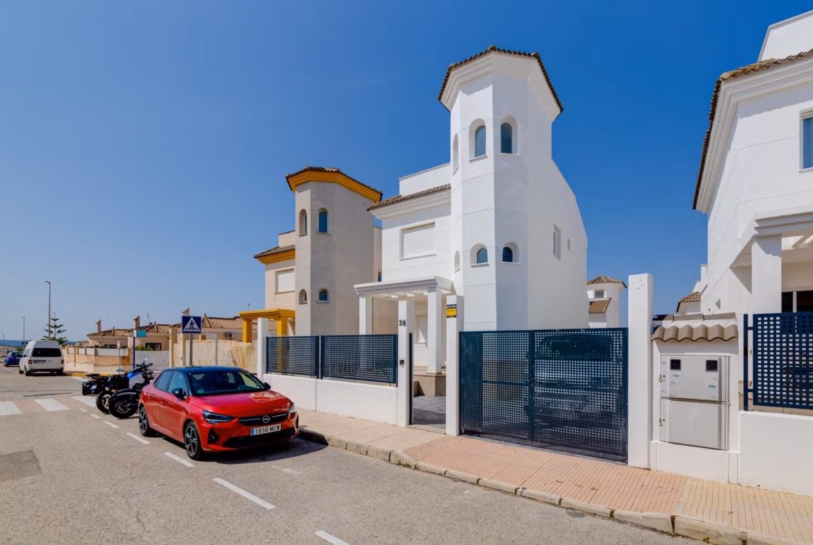 Bright, modern 3-bedroom villa with elegant white façade and gated entrance in sunlit El Oasis, San Fulgencio neighborhood.