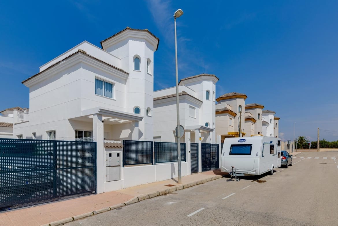 Modern white three-bedroom villas with elegant tiled roofs and gated gardens in sunny El Oasis, San Fulgencio street view