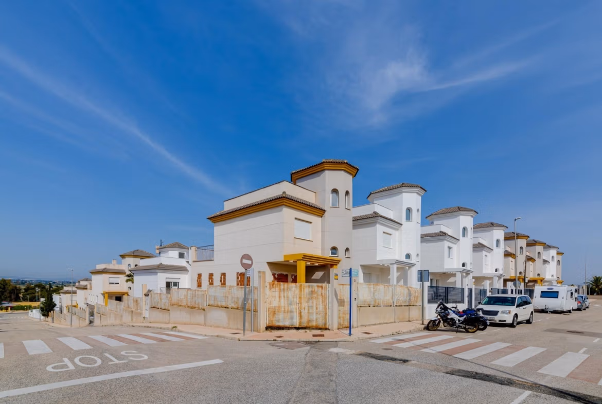 NEW-BUILD-RESIDENTIAL-IN-SAN-FULGENCIO-41 Bright, elegant 2-bedroom semi-detached villa in El Oasis La Marina Urbanisation with modern exterior and clear blue sky backdrop.