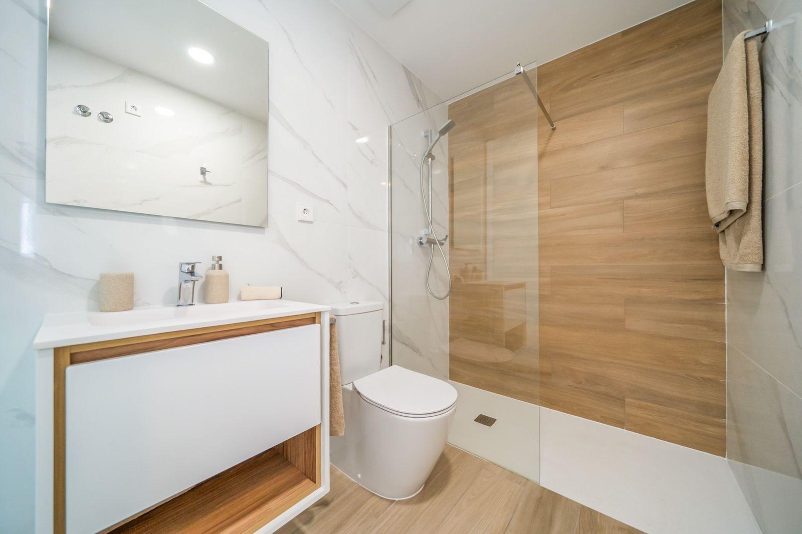 Modern 2-bedroom townhouse bathroom in Vistabella Golf, Orihuela with sleek wood and marble finishes and walk-in glass shower.