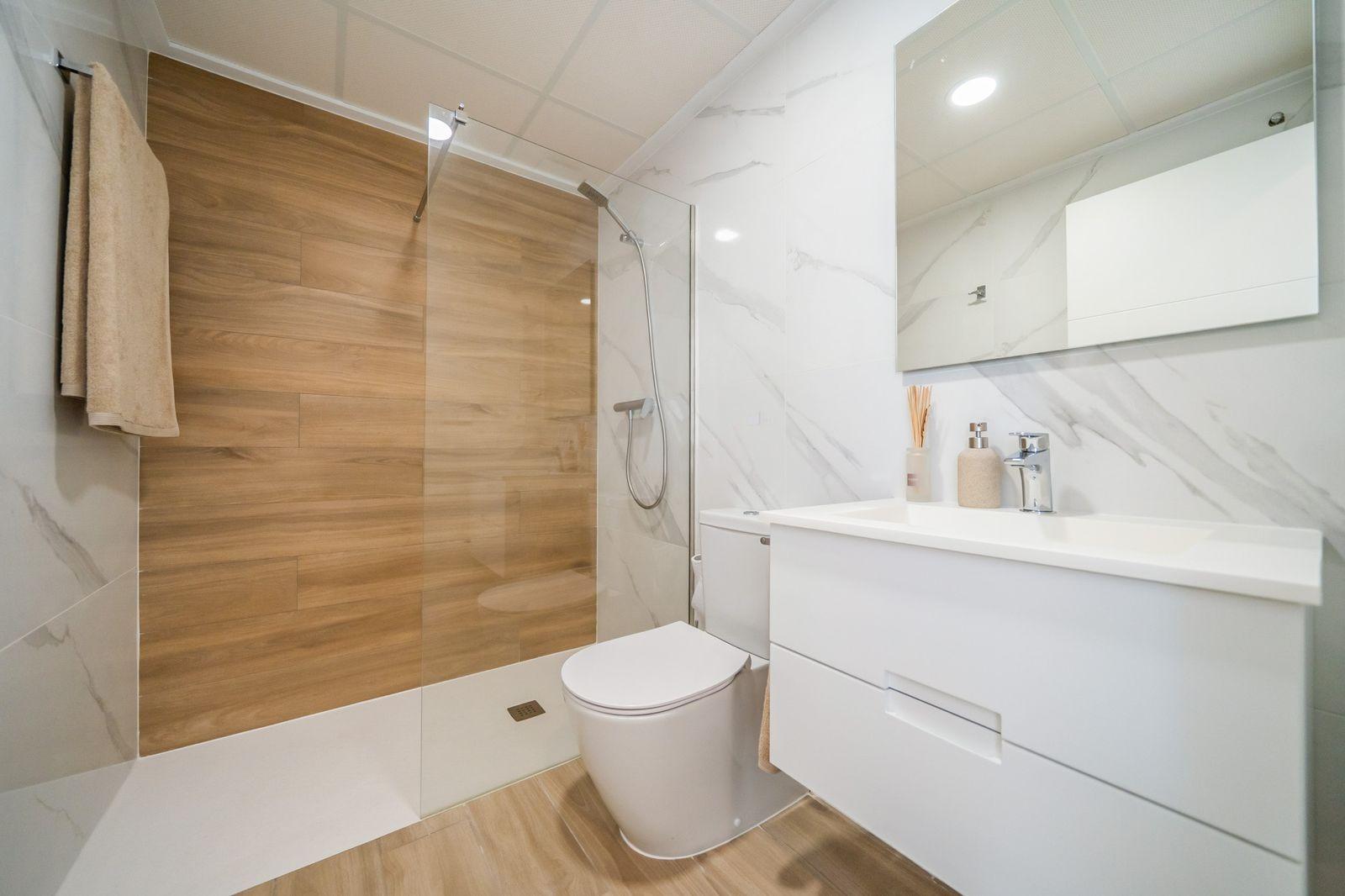 NEW-BUILD-RESIDENTIAL-OF-BUNGALOW-APARTMENTS-IN-VISTABELLA-16 Modern top floor bungalow bathroom in Vistabella Golf Orihuela with sleek, bright design and elegant wood-accented shower area.