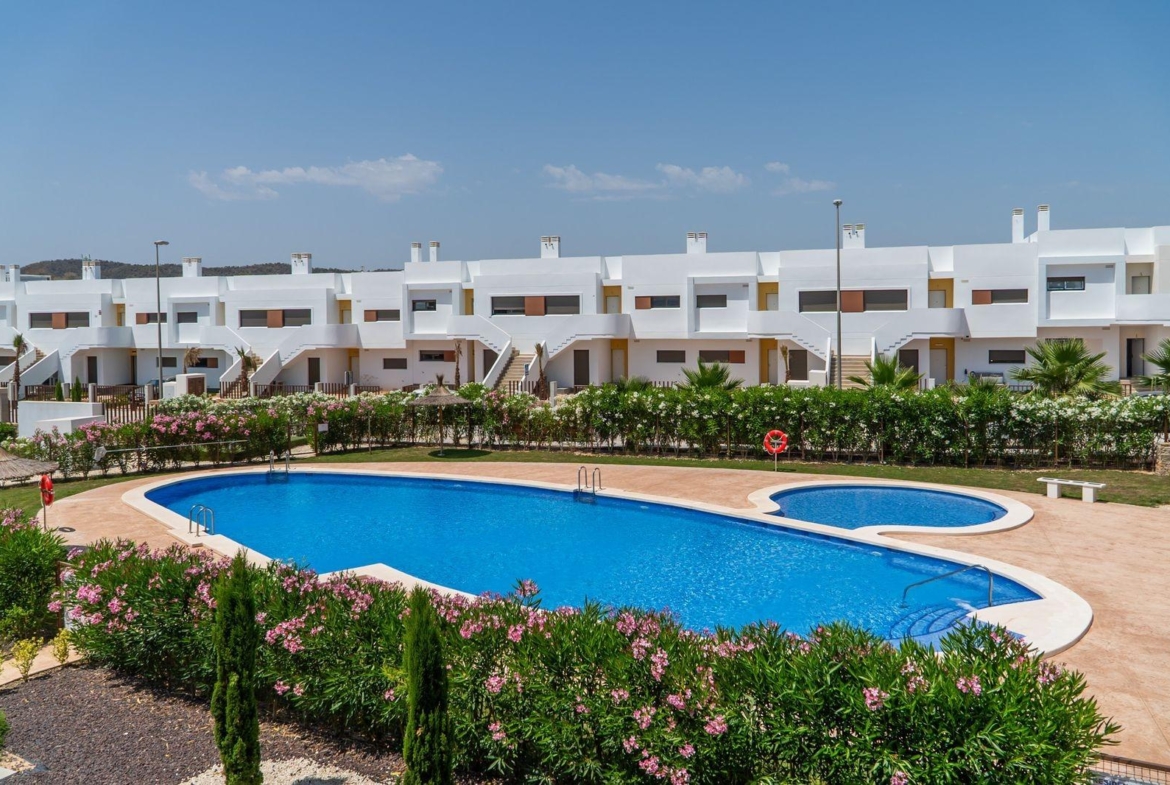 Sun-drenched communal pool with landscaped gardens in front of modern 2-bedroom top floor bungalows at Vistabella Golf, Orihuela