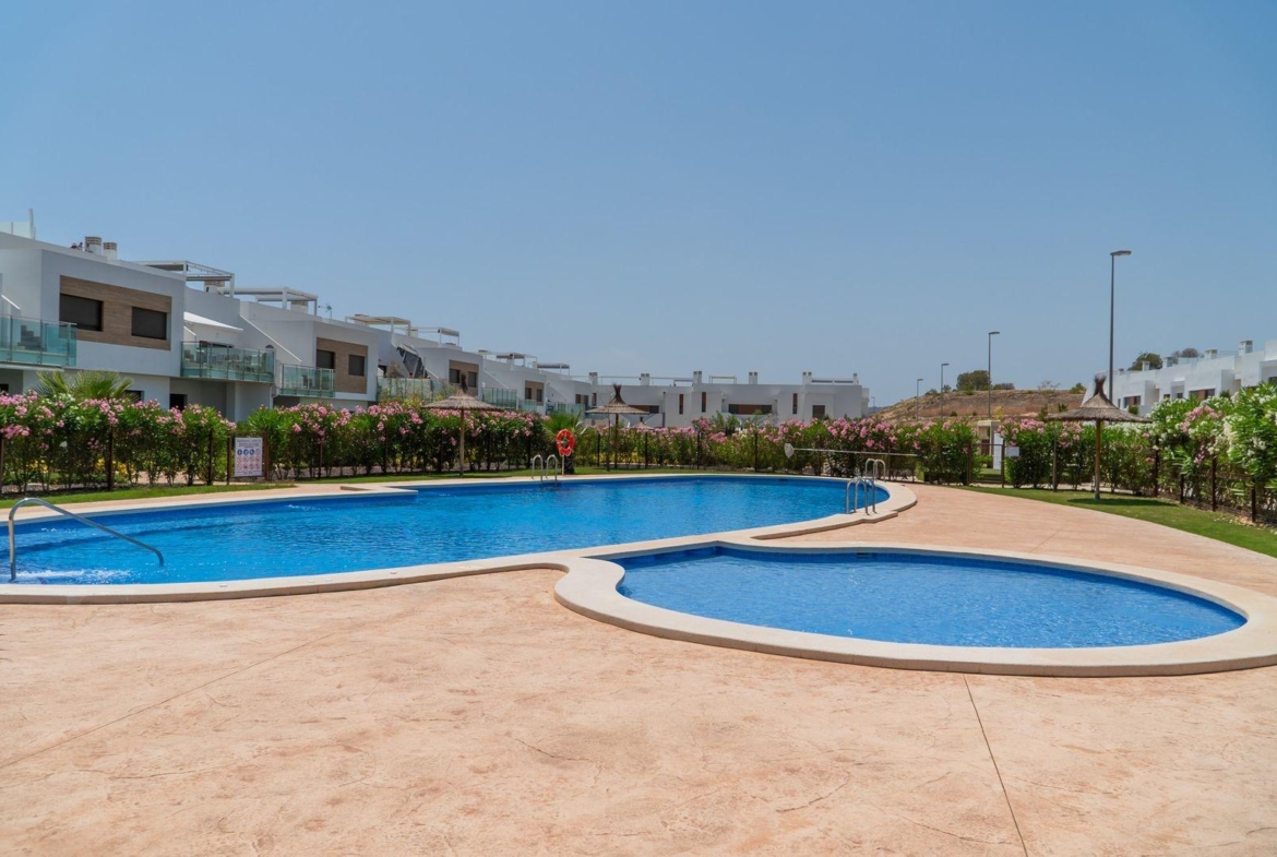 Sun-drenched communal pool with landscaped gardens in front of modern 2-bedroom top floor bungalow in Vistabella Golf, Orihuela