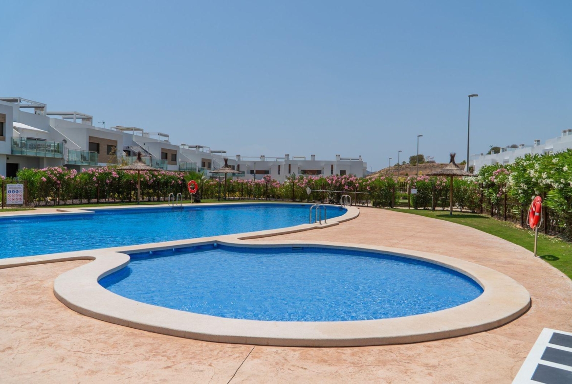 Sparkling blue swimming pools surrounded by landscaped gardens at a modern 2-bedroom top floor bungalow in Vistabella Golf, Orihuela