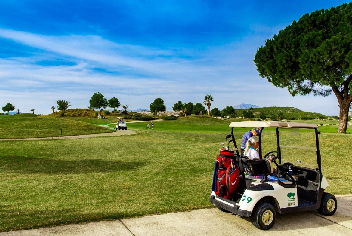 Sunlit golf course view with a modern golf cart, surrounding greenery from the top floor 2-bedroom apartment at Vistabella Golf, Orihuela.