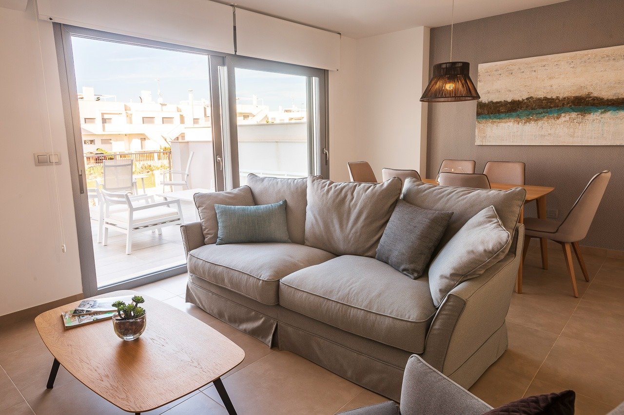 Bright, modern living area with plush sofa and dining space opening onto a sunny terrace in a 2-bedroom top floor apartment in Vistabella Golf, Orihuela.