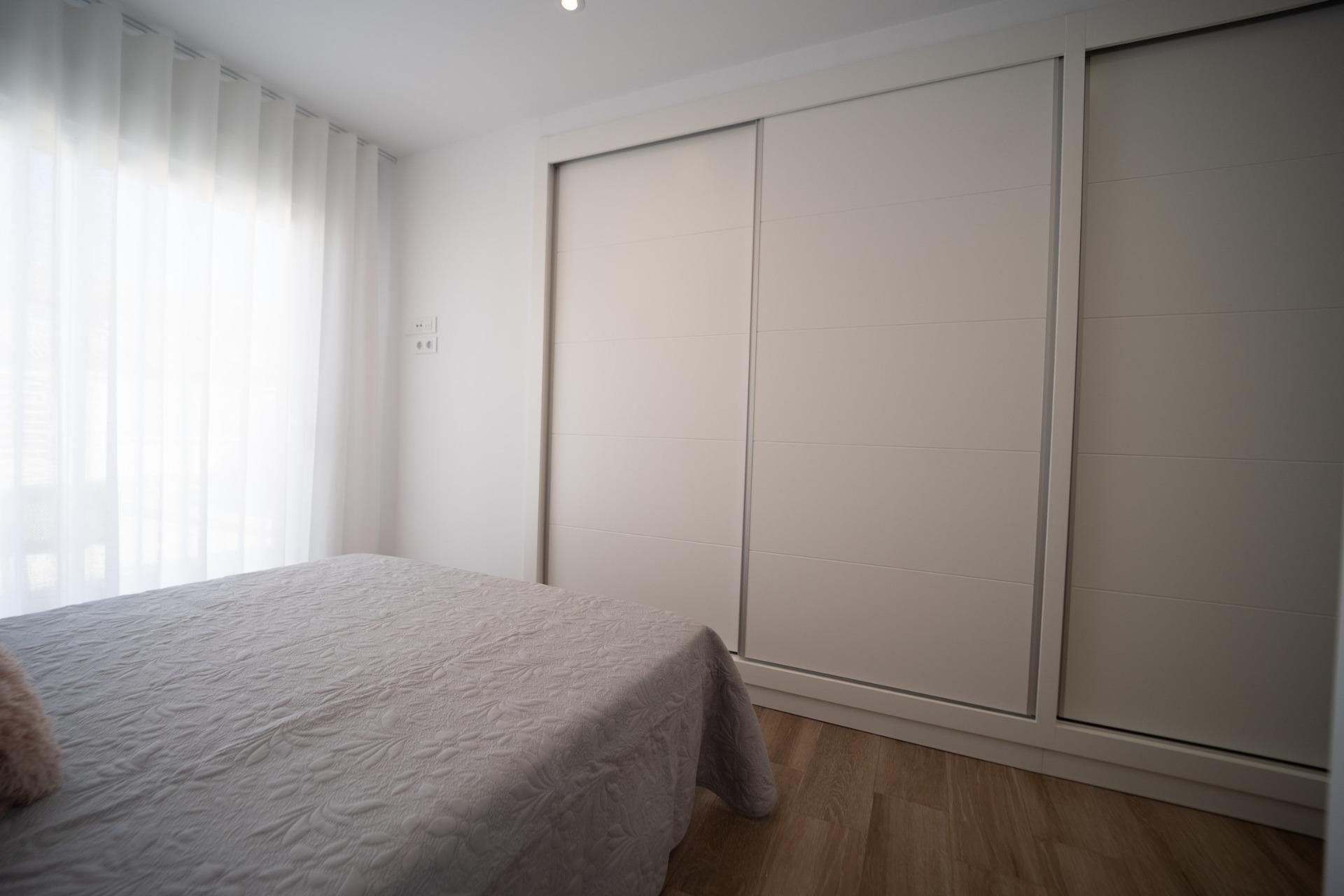 NEW-BUILD-TOWNHOUSES-IN-SAN-JAVIER-14 Bright and modern bedroom in new build townhouses in San Javier with elegant sliding wardrobes and soft natural light filtering through sheer curtains.
