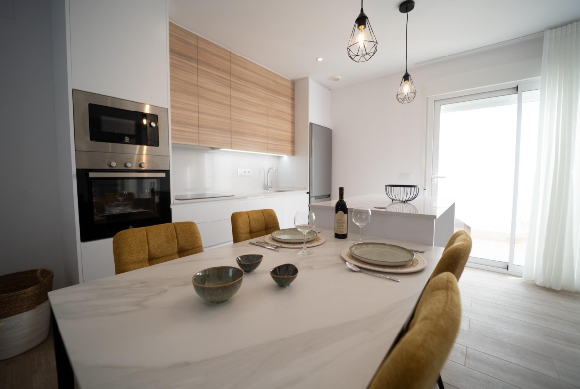 Bright modern kitchen with elegant wood cabinets and marble dining table in new build townhouses in San Javier